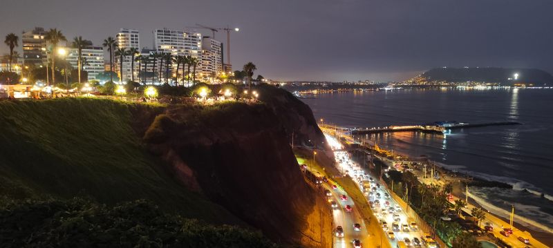 Los edificios iluminados de Miraflores se asoman a la Costa Verde con el denso tráfico, a sus pies, delimitando la línea de costa.